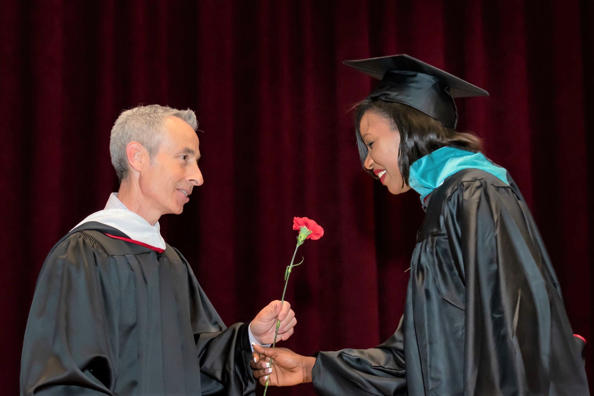 University College Dean Michael McGuire hands a carnation to a smiling graduate