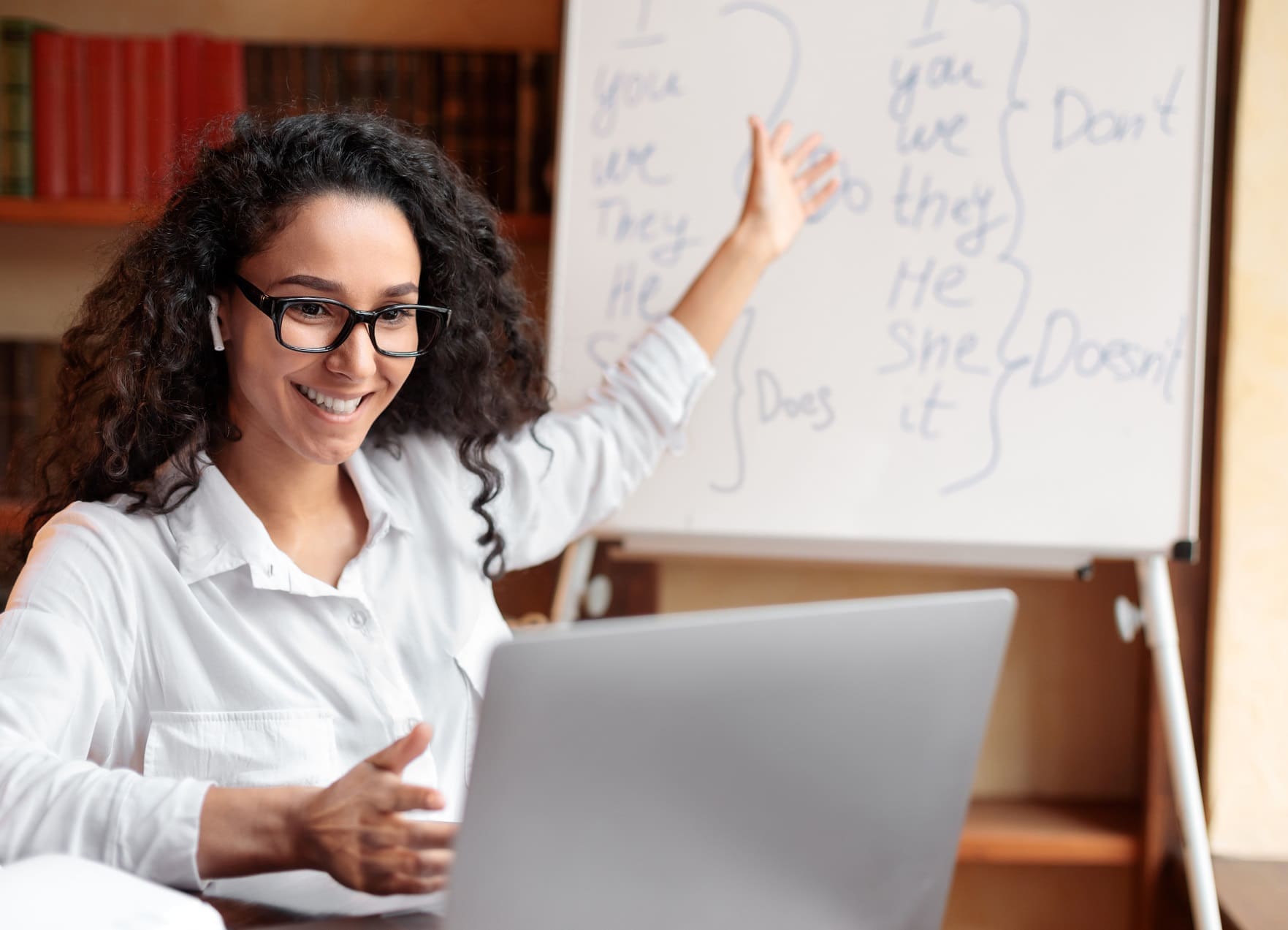 An instructor gestures to a visual aid behind her while teaching an online class on her laptop